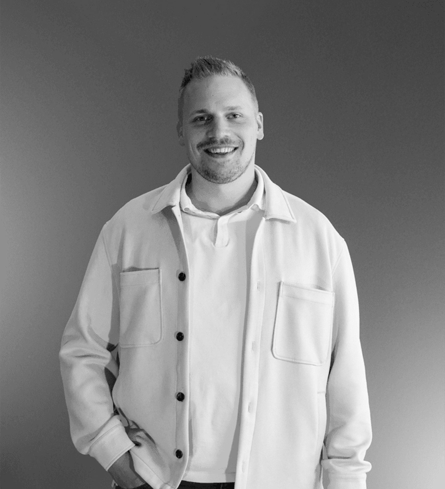 Over ons 5 Een glimlachende man met kort haar en een getrimde baard staat tegen een effen achtergrond. Hij is netjes gekleed en straalt zelfvertrouwen uit - een ideaal portret voor rijnders webdesign, stijlvol vastgelegd in zwart-wit.