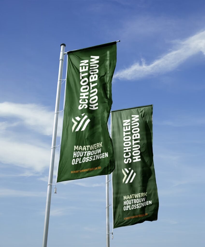 Twee hoge groene vlaggen met witte tekst "schooten houtbouw" en "maatwerk houtbouw oplossingen" wapperen aan vlaggenmasten tegen een blauwe lucht, met het geometrische logo van schooten houtbouw en de url van de website.